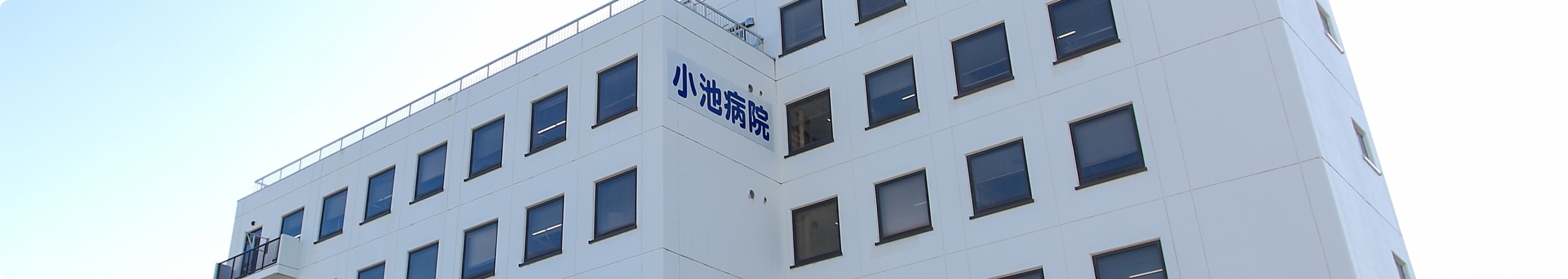白い4階建ての医療施設外観。規則的に配置された窓と屋上手すり。